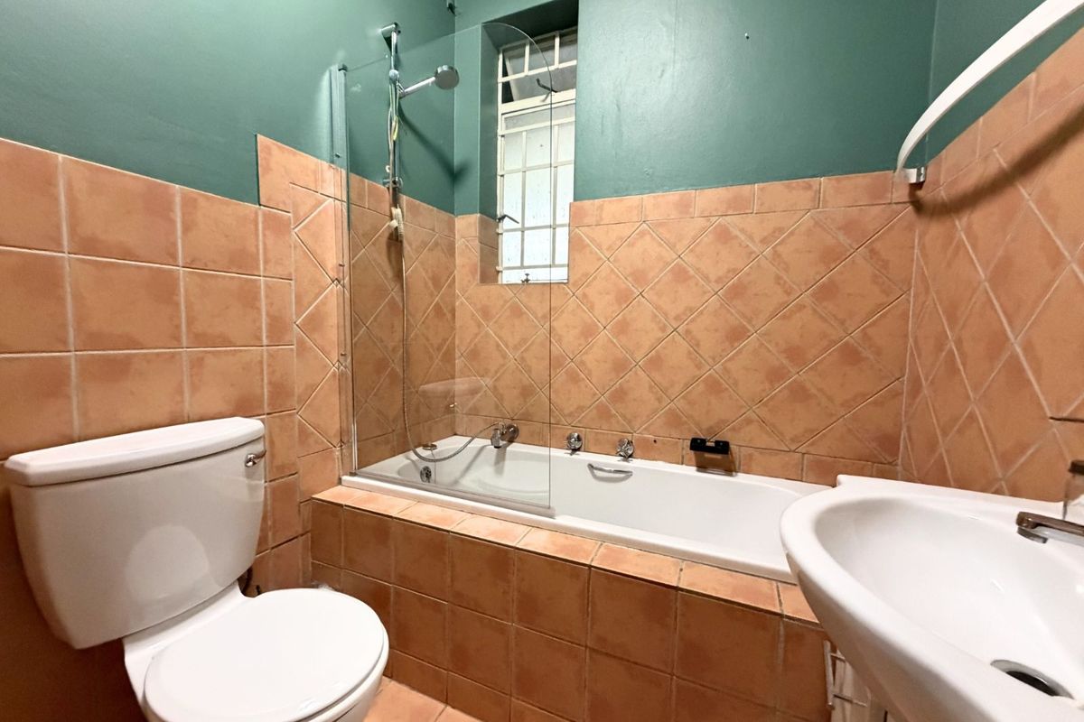 A functional bathroom featuring a built-in bathtub with a glass shower screen, a pedestal basin, and a toilet, finished with terracotta-style wall tiling.