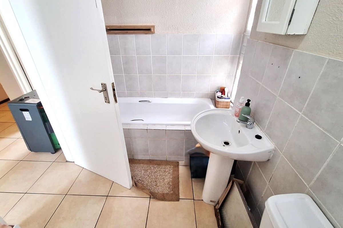 A functional bathroom featuring a built-in bathtub, pedestal basin, and tiled walls and flooring.