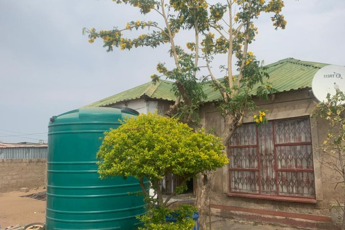 Exterior view of the property featuring a green water storage tank, established garden, and metal security bars on the windows.