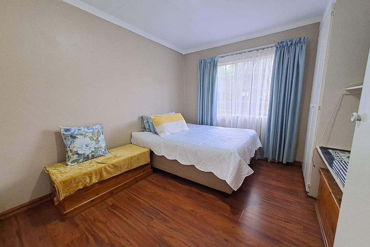 A bedroom featuring wood-look flooring, built-in cupboards, and a window with curtains.