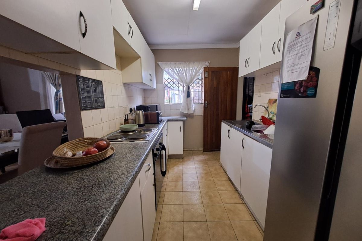 Functional galley-style kitchen featuring granite countertops, white cabinetry, built-in hob and oven, and tiled flooring.