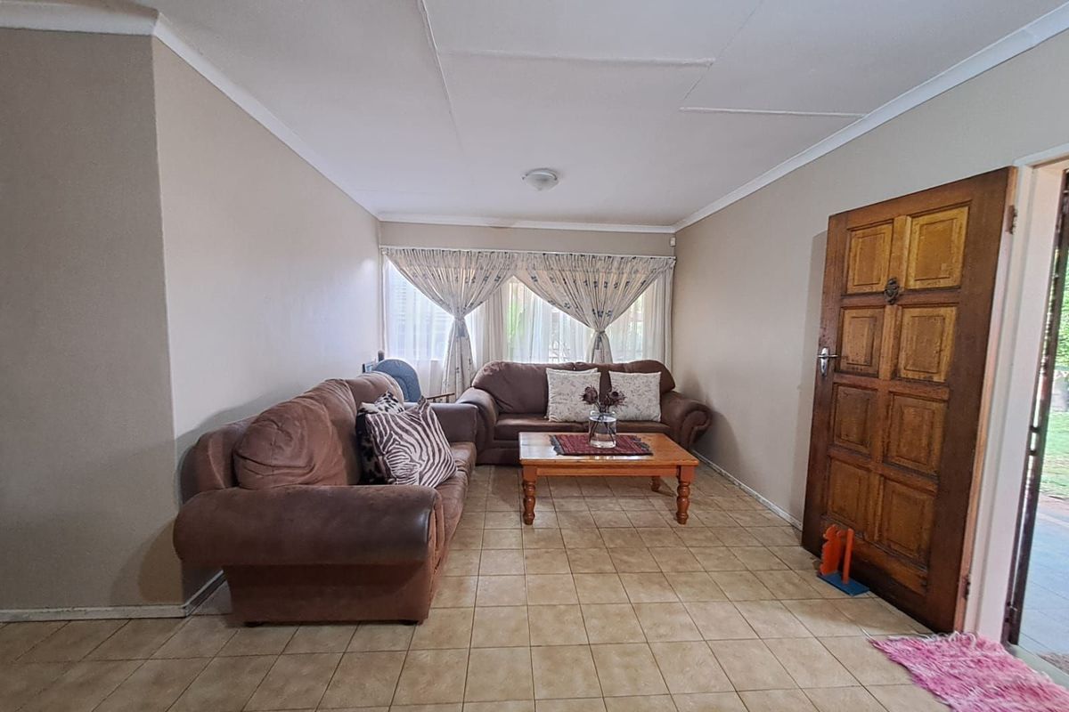 A living room featuring tiled flooring, a solid timber entrance door, and large windows with curtains, providing a functional and lived-in space.