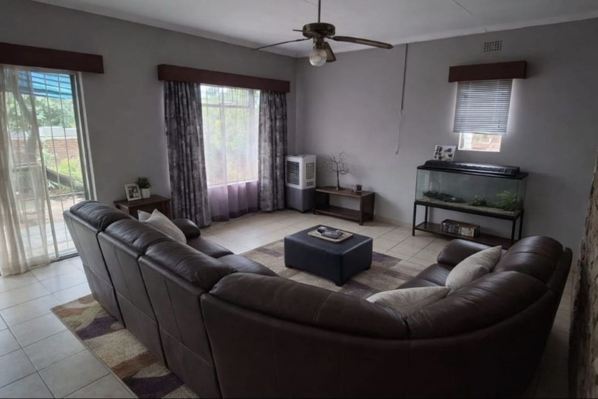 A spacious living room featuring tiled flooring, a ceiling fan, and large windows providing natural light with access to an outdoor area.