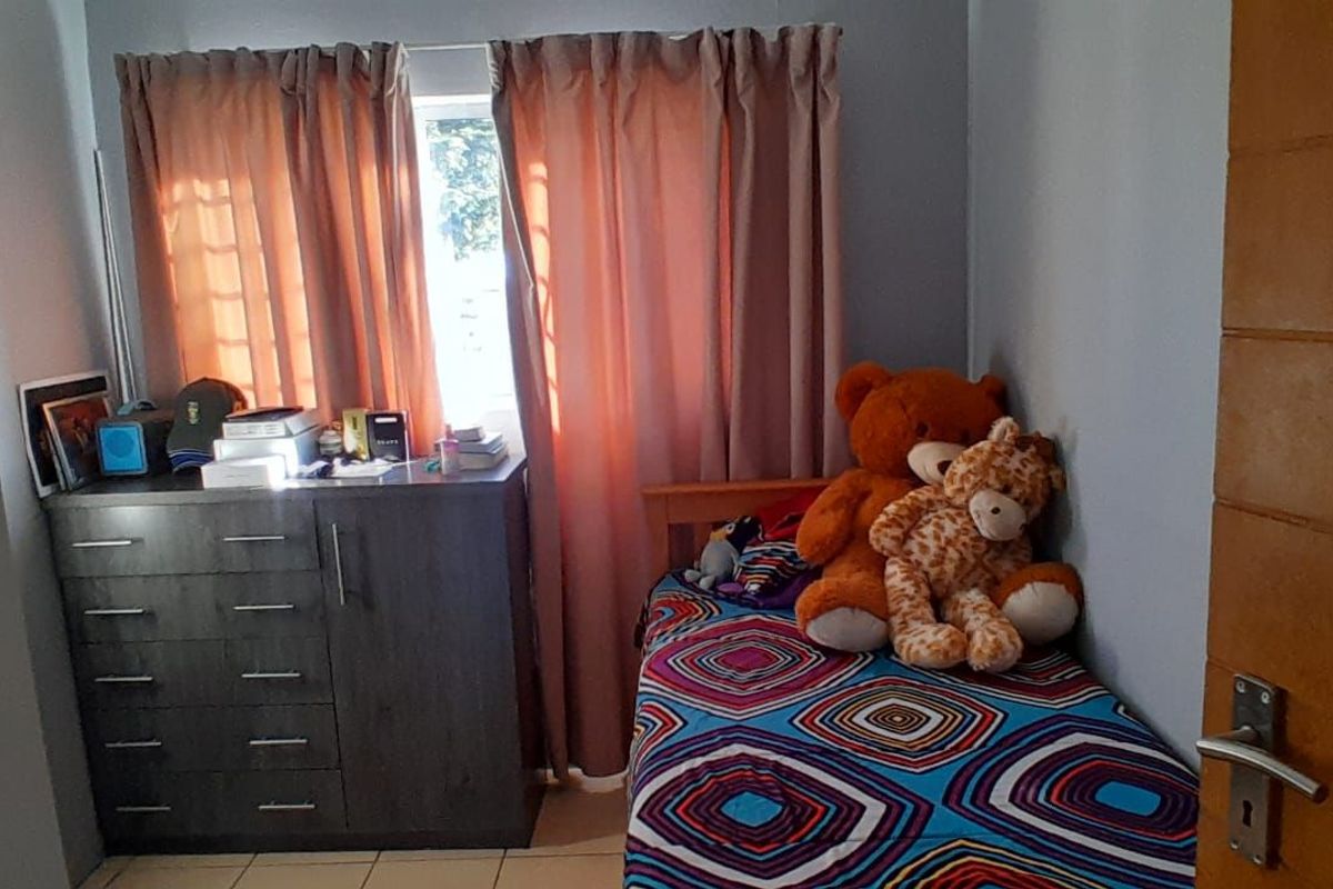 A functional bedroom featuring tiled flooring, a window with curtains, and a wooden door.