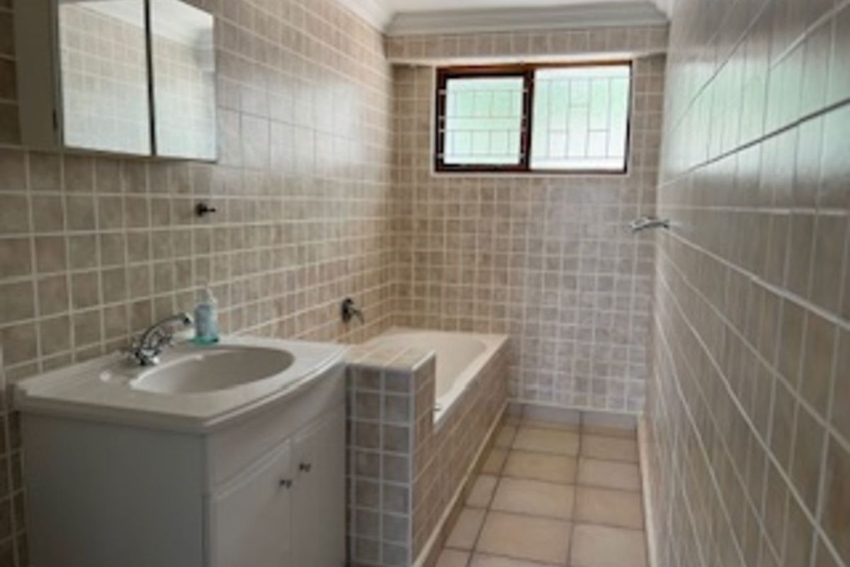 A functional bathroom featuring a built-in bathtub, a vanity cabinet with a basin, and full-height wall tiling.
