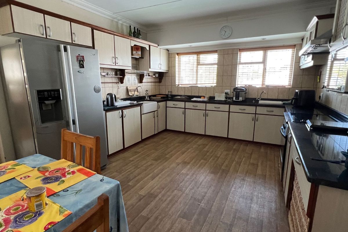 A functional kitchen featuring ample cabinetry, dark countertops, a farmhouse-style sink, and integrated extractor fan, with wood-look flooring throughout.