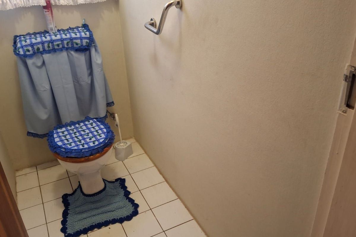 A small bathroom featuring a standard toilet, tiled flooring, and a wall-mounted grab rail for accessibility.