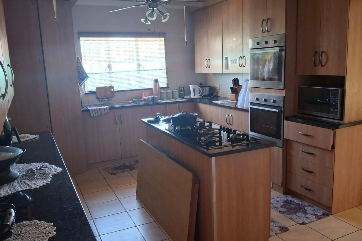 A functional kitchen featuring wood-look cabinetry, granite countertops, a central island with a gas hob, and built-in double ovens.
