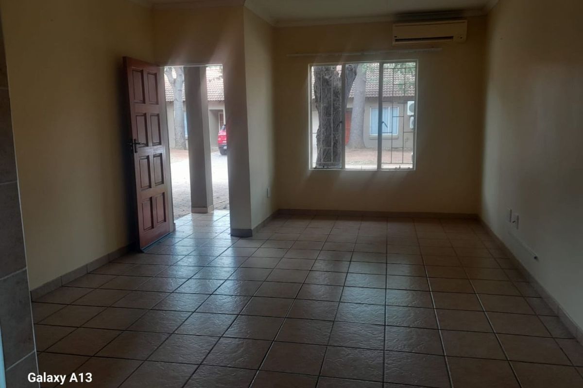 An empty living room featuring tiled flooring, a wall-mounted air conditioning unit, and a wooden entrance door leading to the exterior.