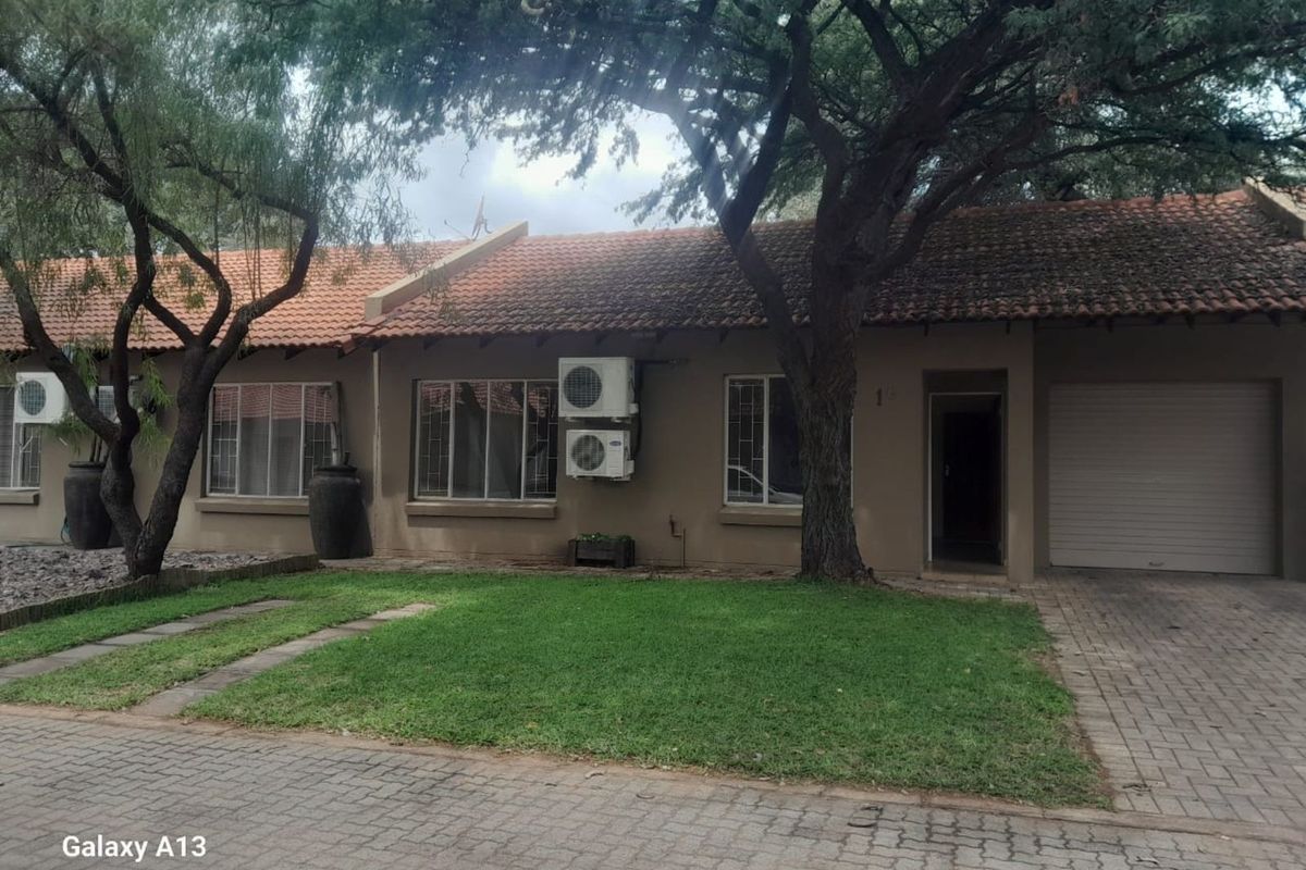Front elevation of a single-story residential house featuring a tiled roof, paved driveway, integrated garage, and established garden area.