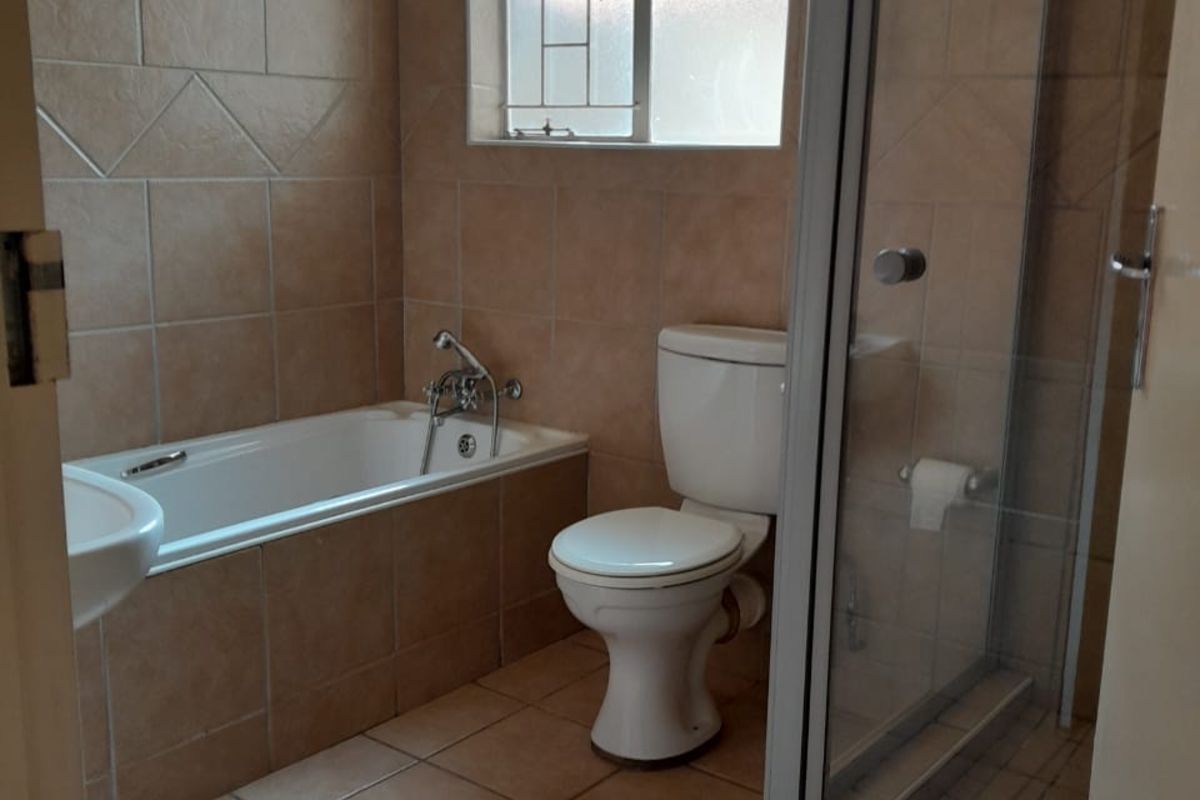 A functional bathroom featuring a built-in bathtub, separate glass-enclosed shower, toilet, and tiled flooring with neutral wall tiling.