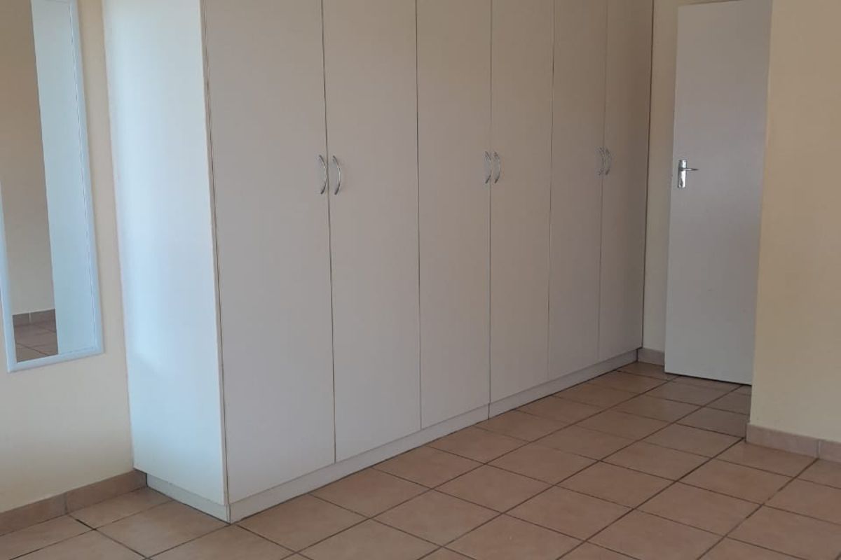A bedroom featuring built-in floor-to-ceiling wardrobes, tiled flooring, and a neutral wall finish.