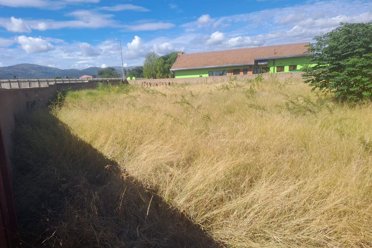 A view of a vacant residential plot featuring perimeter boundary walls and overgrown grass, situated in a developed neighborhood.