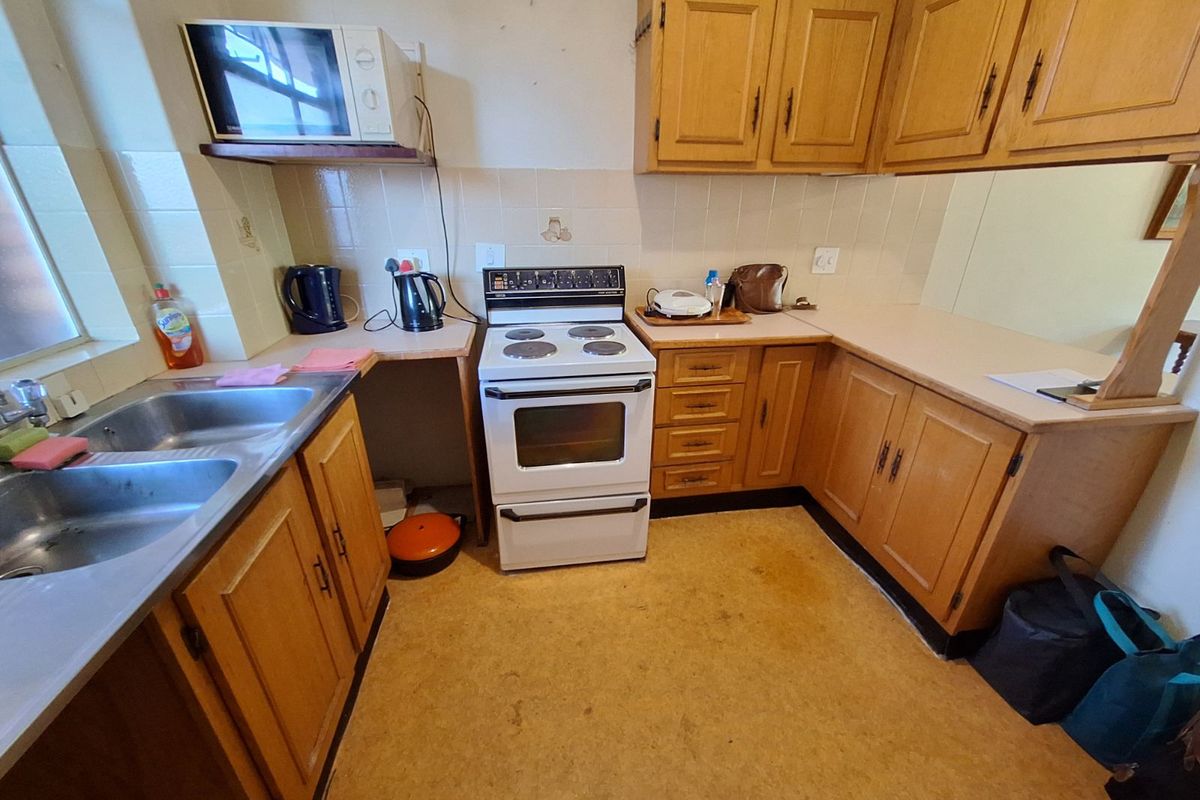 A dated kitchen featuring wooden cabinetry, a freestanding electric stove, double stainless steel sink, and tiled splashbacks.