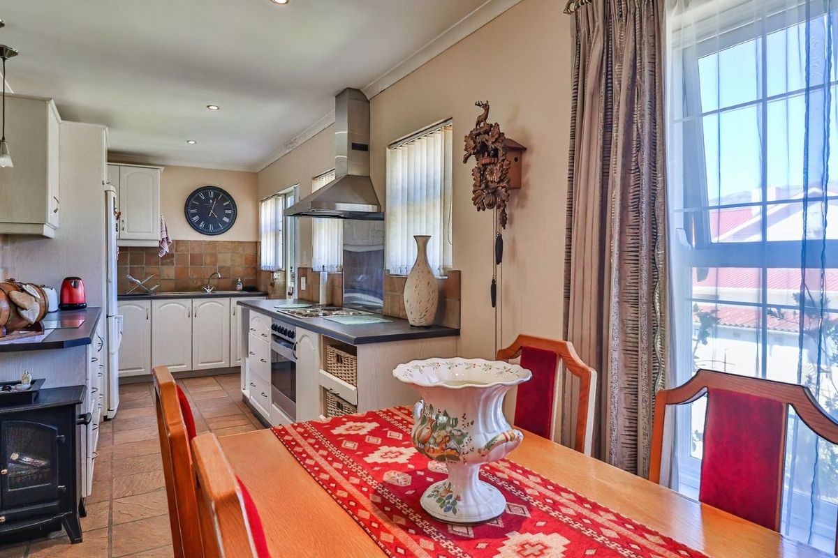 A functional kitchen featuring built-in cabinetry, tiled backsplash, integrated oven and hob, and tiled flooring, adjacent to a dining area.