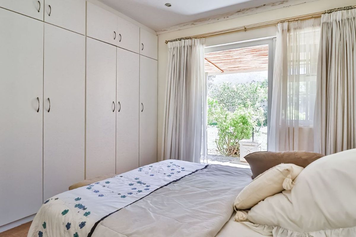 A bright bedroom featuring extensive floor-to-ceiling built-in cupboards and a sliding glass door providing direct access to the garden.