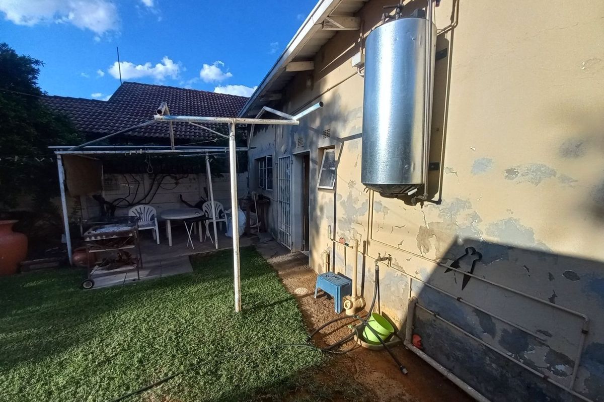 Rear exterior view of the property featuring a mounted geyser, exposed plumbing, and a small paved patio area adjacent to the garden.