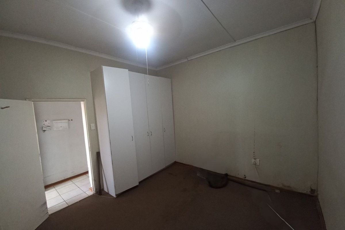 A vacant bedroom featuring built-in white cabinetry, neutral wall finishes, and carpeted flooring, requiring cosmetic updates to restore its appeal.