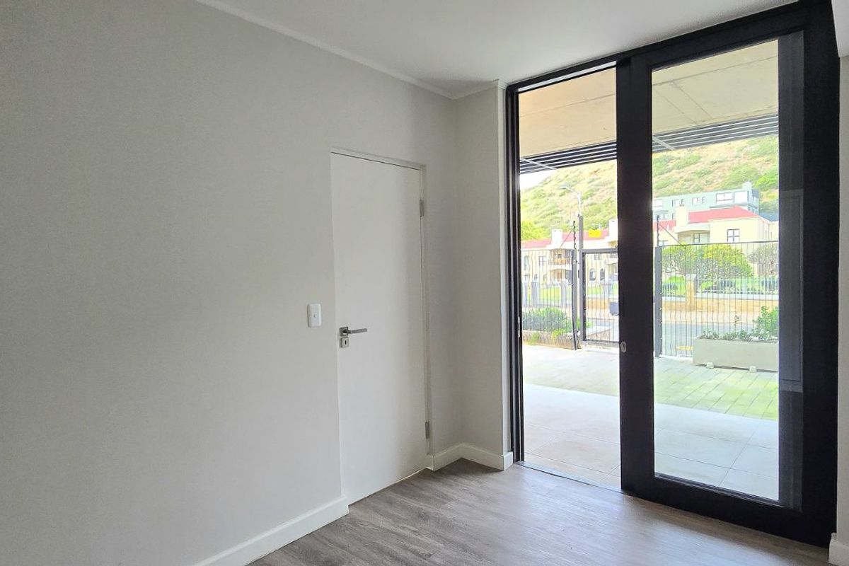 A bright, empty room featuring modern wood-look flooring and a large sliding glass door providing direct access to an outdoor patio area.