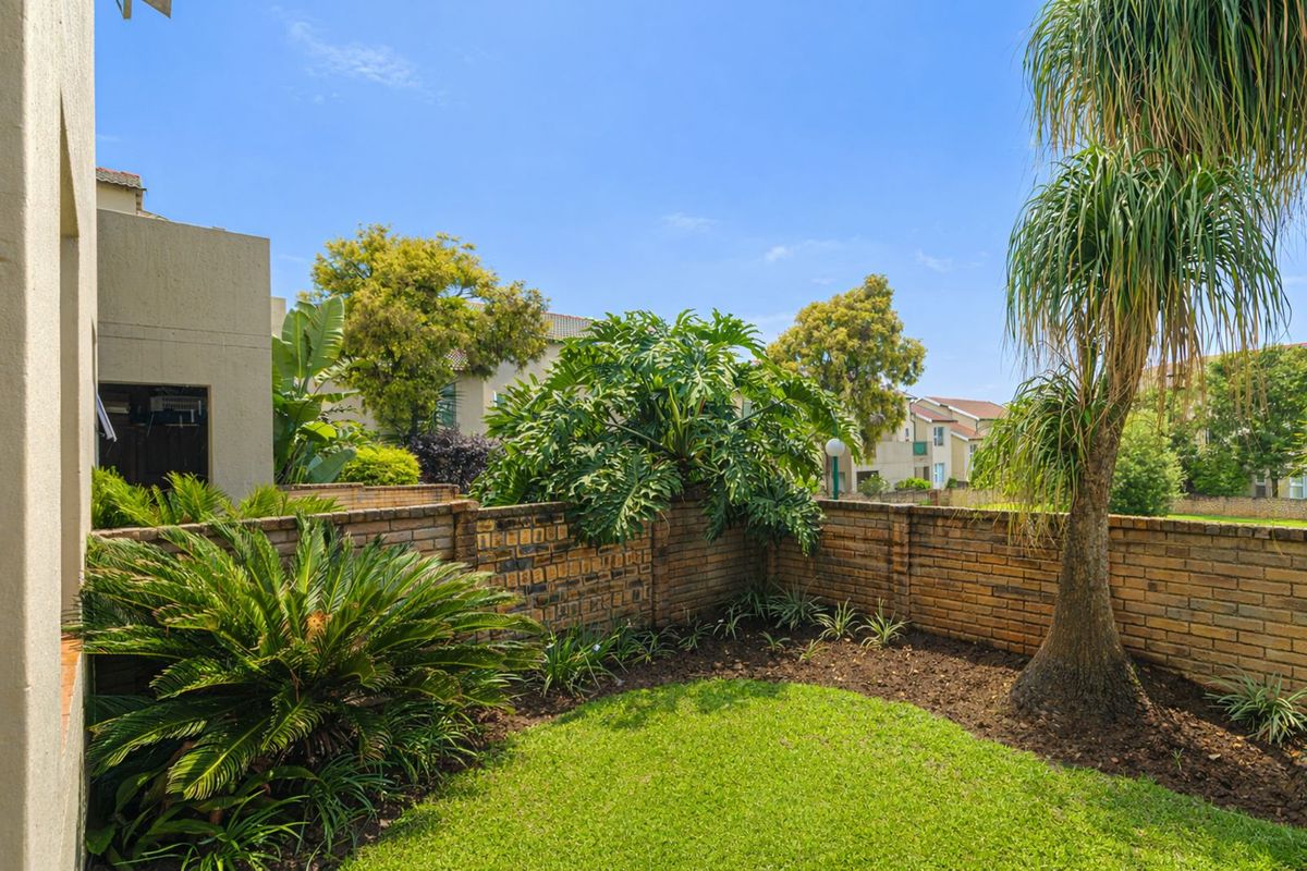 A private rear garden featuring a manicured lawn, established tropical landscaping, and a perimeter brick boundary wall.