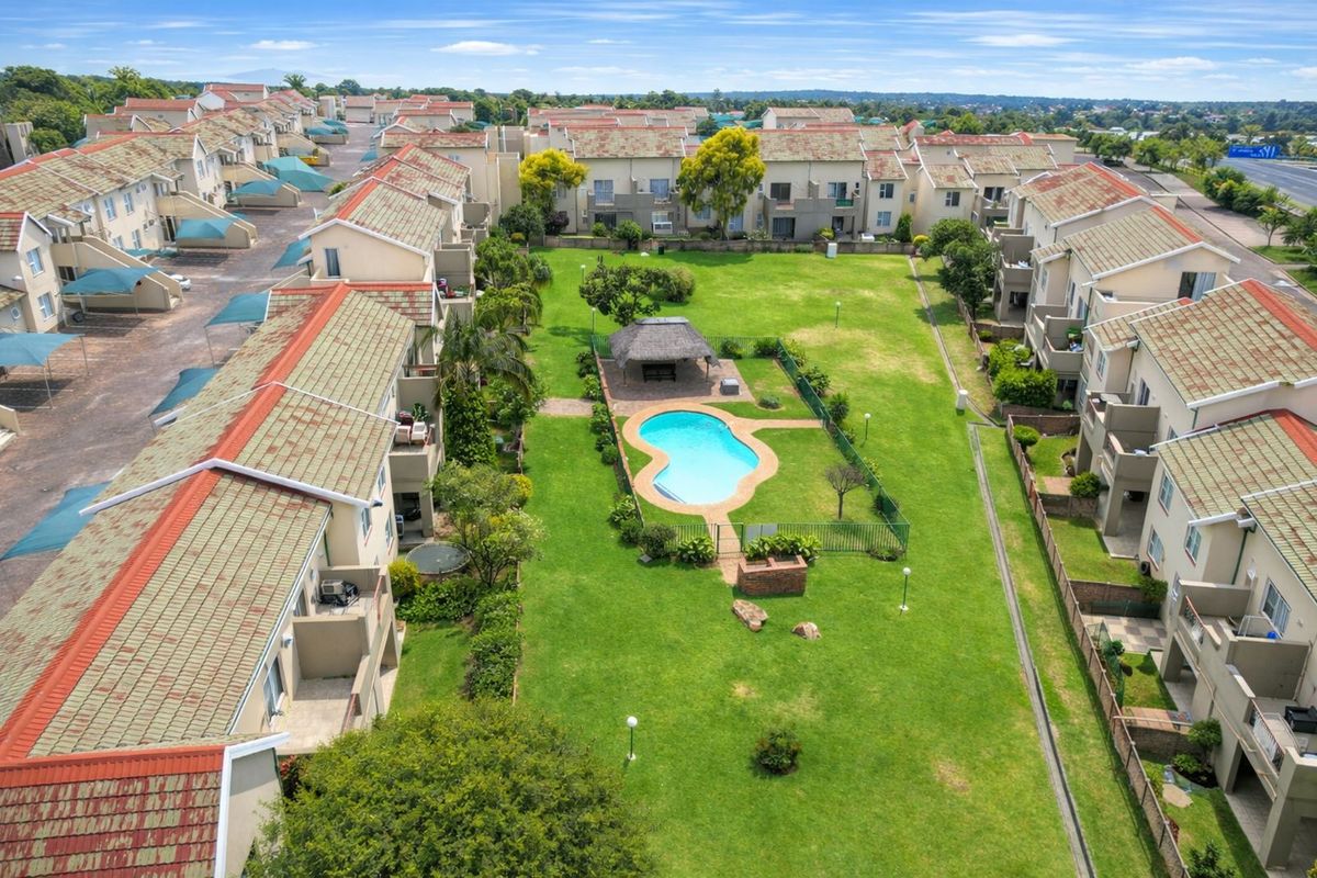 Aerial view of the apartment complex featuring a central communal garden, swimming pool, and thatched gazebo area surrounded by residential units.