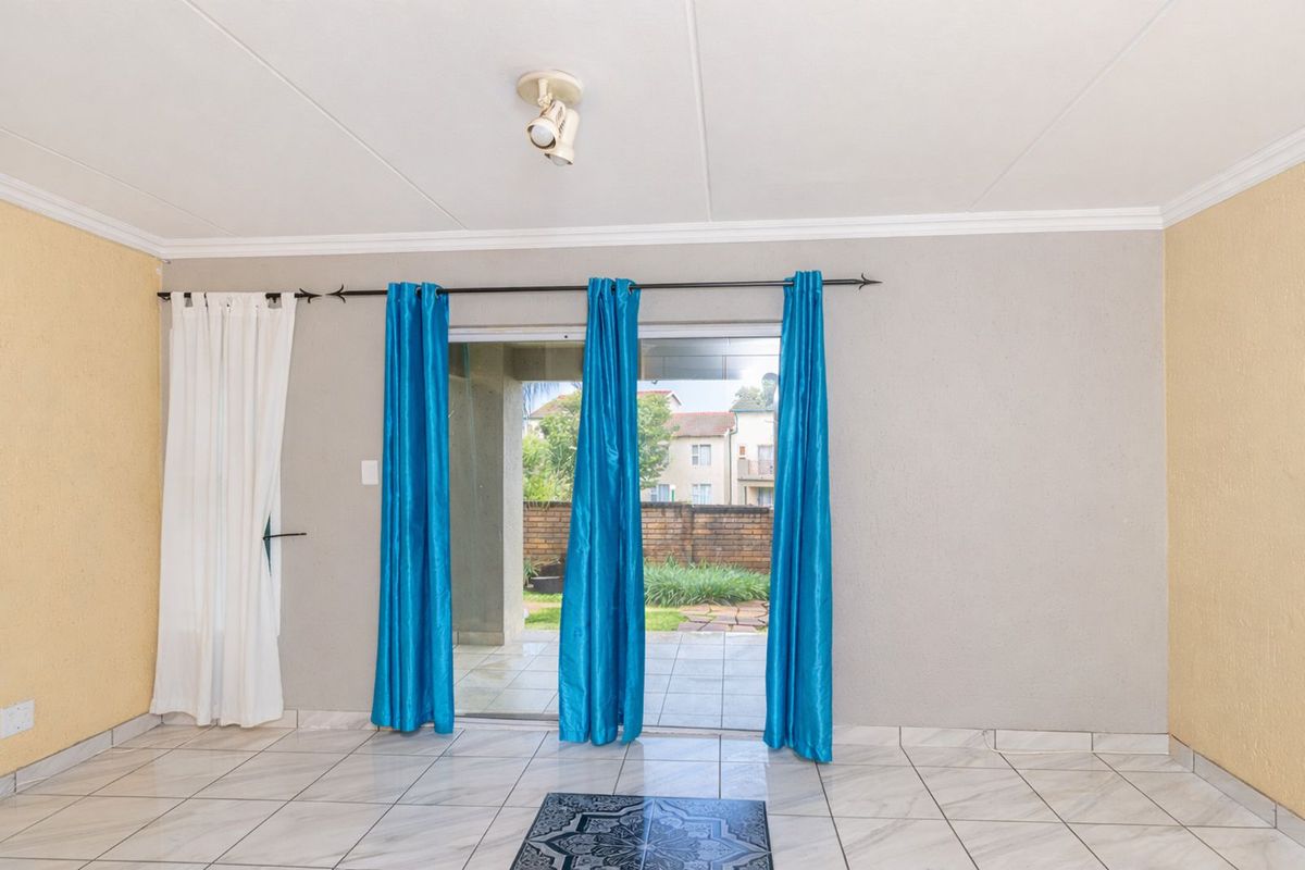 A bright living area featuring tiled flooring and a sliding glass door that opens onto a covered patio and garden.