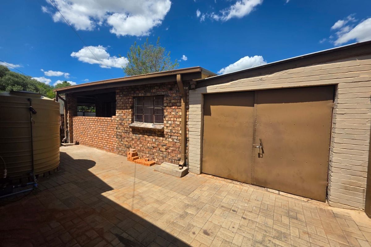 Exterior view of a brick-built garage and adjacent utility area featuring paved flooring and a large water storage tank.