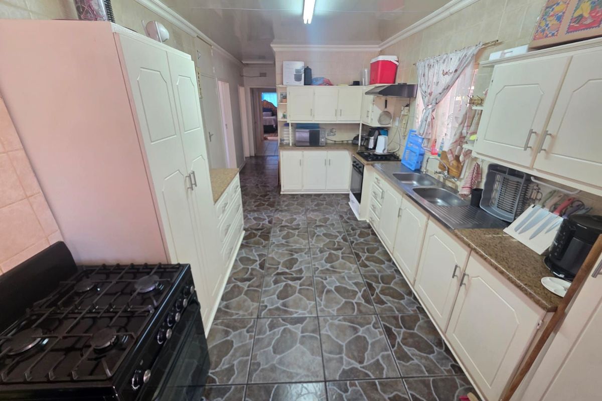 A functional kitchen featuring tiled flooring, ample built-in cabinetry, a double sink, and a gas stove, offering a practical layout for daily meal preparation.