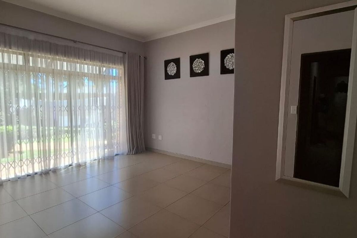 A bright and spacious living area featuring large sliding glass doors with security gates, neutral tiled flooring, and a built-in wall mirror.