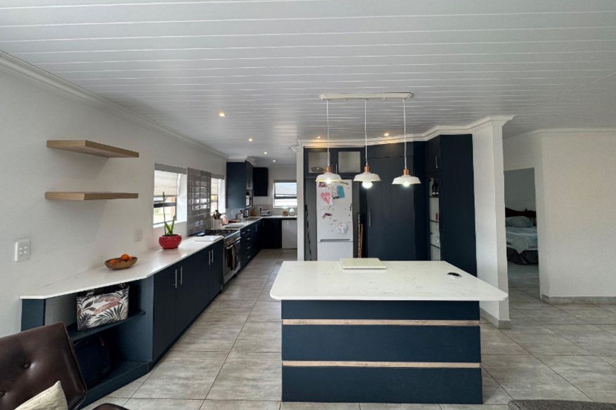 Modern open-plan kitchen featuring dark cabinetry, a central island with stone countertop, and integrated lighting.