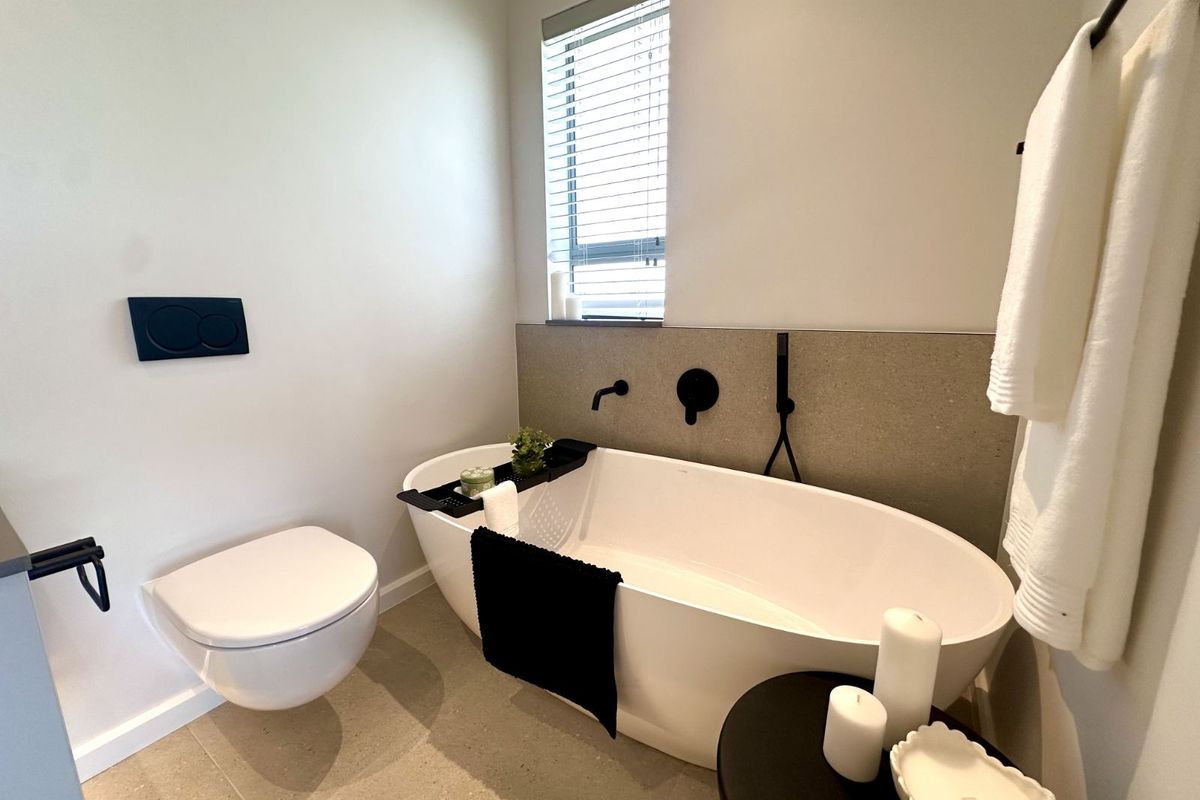 Modern bathroom featuring a sleek freestanding bathtub, wall-mounted toilet, and contemporary matte black fixtures with neutral tiled finishes.
