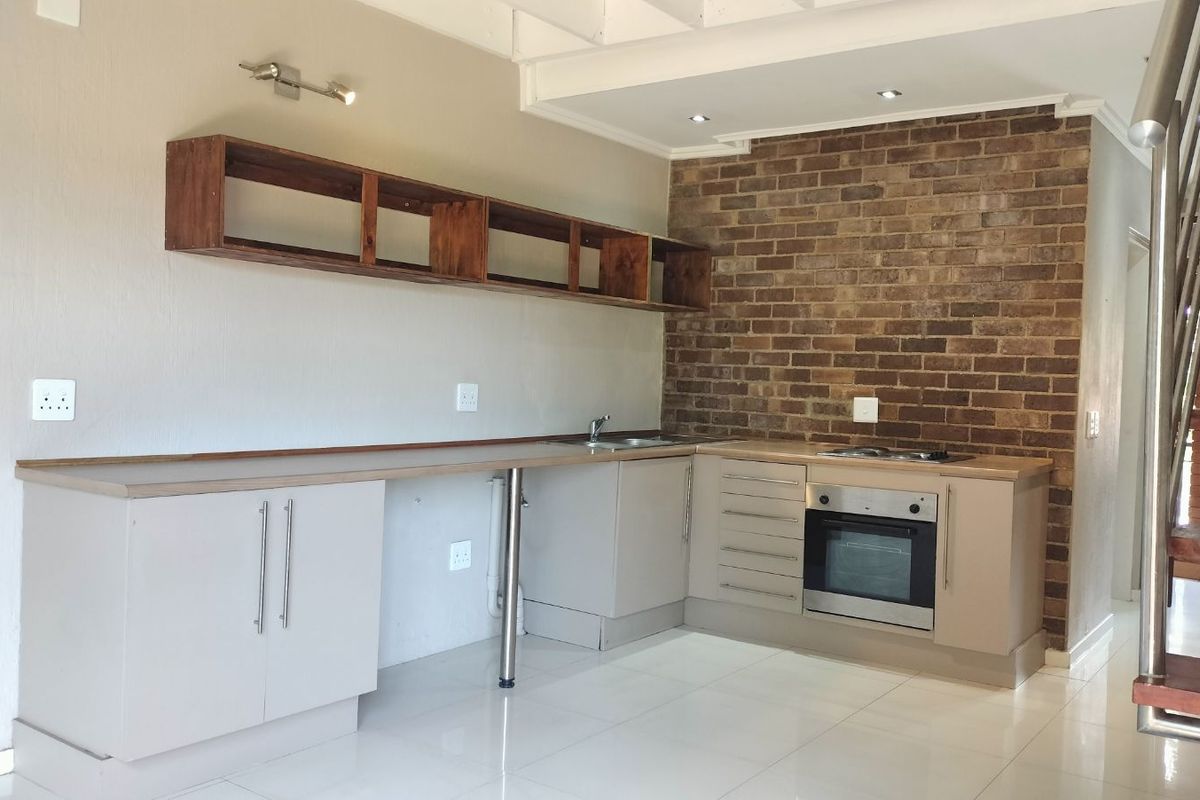 Modern kitchen featuring light-toned cabinetry, a built-in oven and hob, exposed brick feature wall, and sleek tiled flooring.