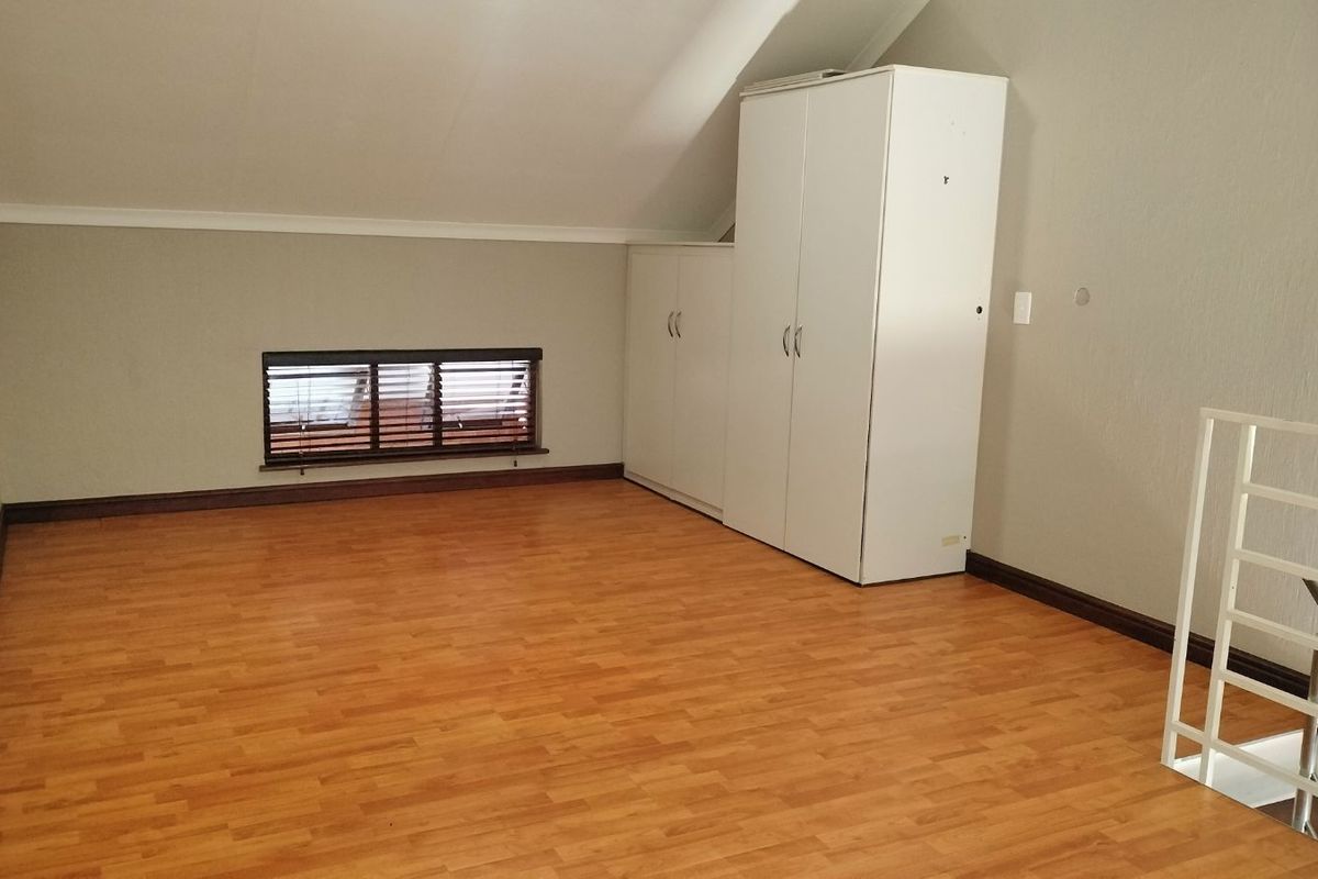 A loft-style bedroom featuring laminate wood flooring, built-in cabinetry, and a sloped ceiling with a small window.