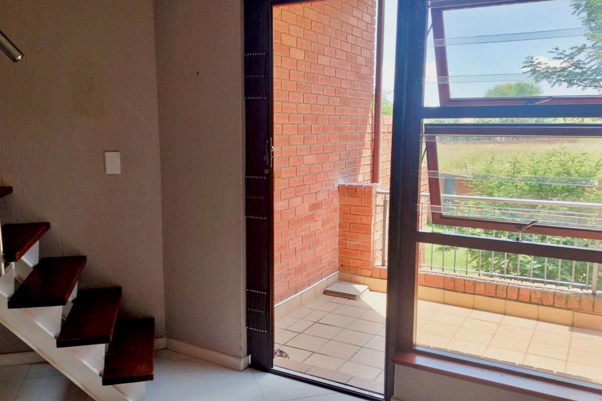 Interior view of a living area featuring a staircase and a doorway leading to a private balcony with brick wall detailing.