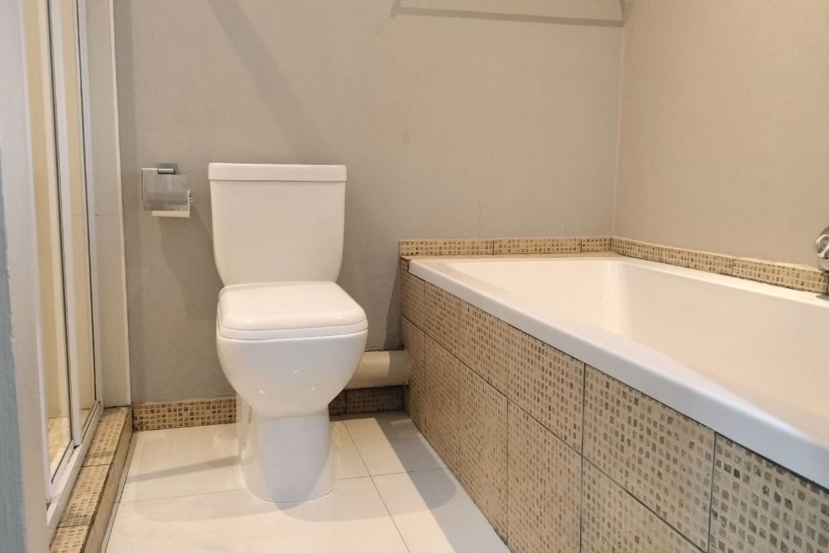 A functional bathroom featuring a tiled bathtub surround, a standard toilet, and a separate shower enclosure with neutral wall finishes.