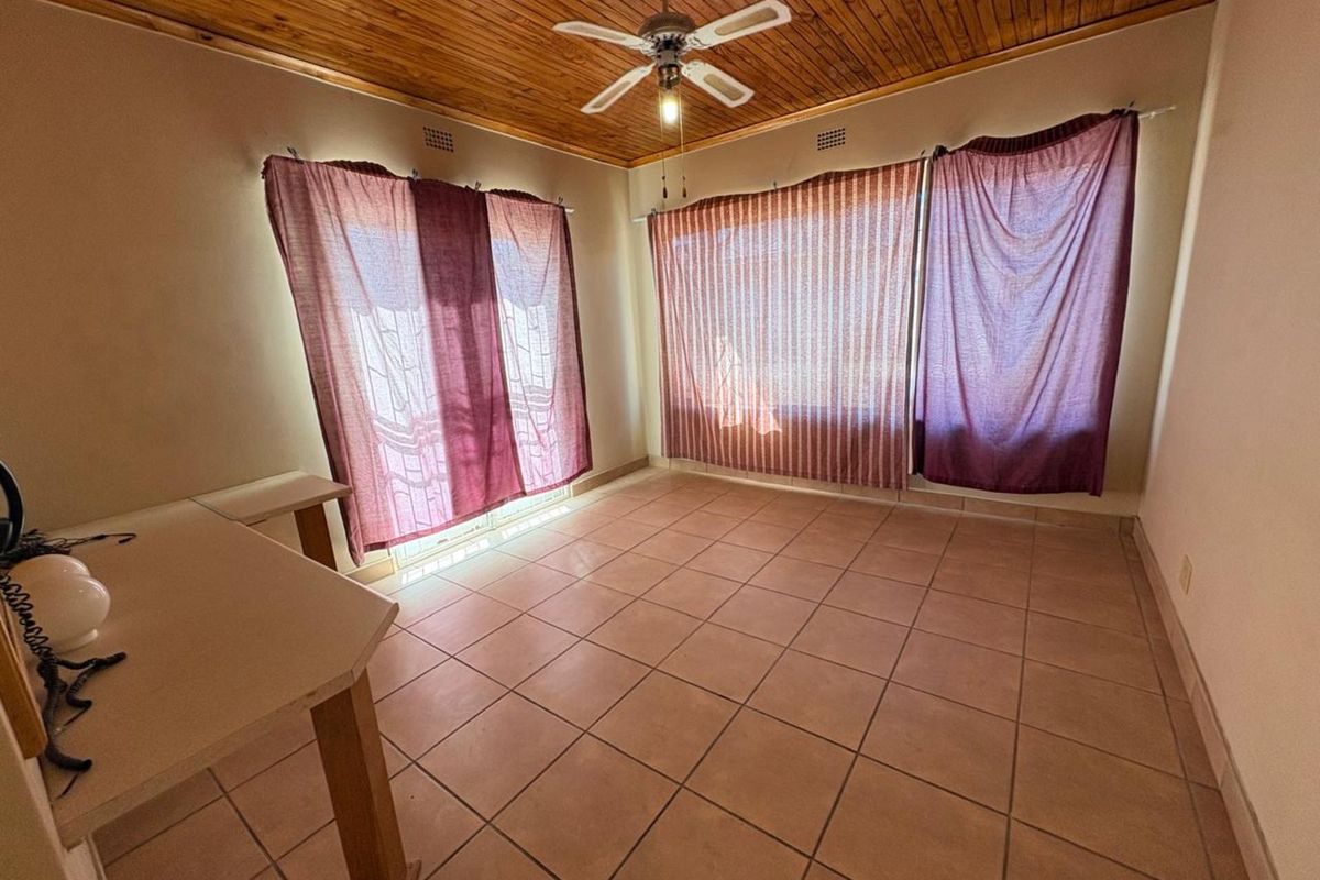 A spacious living room featuring tiled flooring, a timber-clad ceiling, and a ceiling fan, offering a versatile area for relaxation.