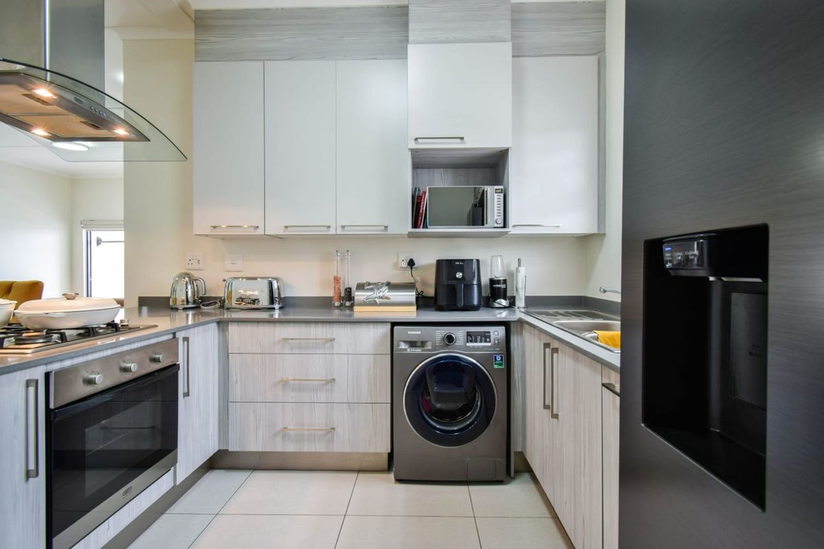 Modern kitchen featuring light wood-grain cabinetry, stone countertops, integrated oven, glass extractor fan, and a built-in washing machine.