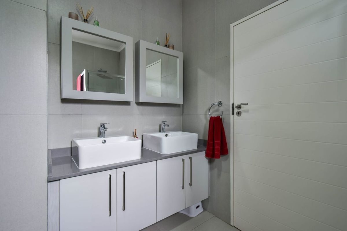 Modern bathroom featuring a double vanity with white vessel sinks, grey stone countertop, white cabinetry, and matching wall-mounted mirrors.