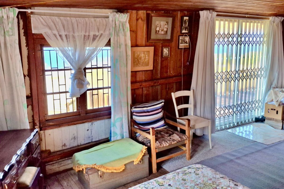 A rustic bedroom featuring timber wall paneling, large windows with security bars, and a sliding door leading to an outdoor area.