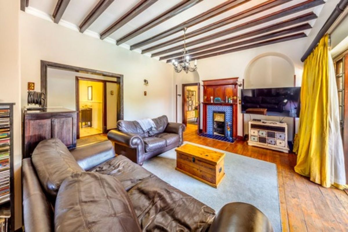 Spacious living room featuring exposed timber ceiling beams, a traditional fireplace with tiled surround, and polished wooden flooring with direct access to adjacent rooms.