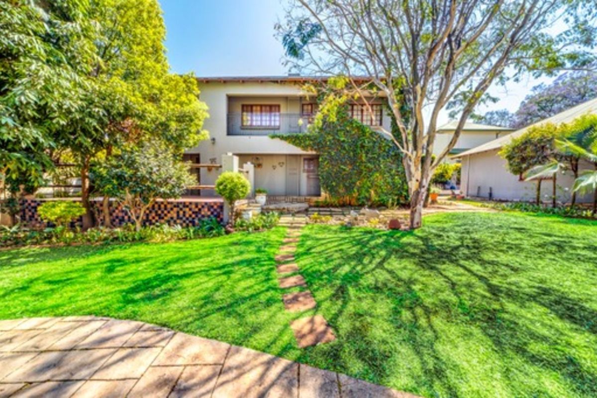 A view of the rear exterior of the property featuring a landscaped garden, mature trees, a stone pathway, and a covered patio area.