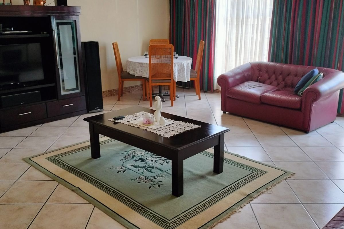 Spacious living area featuring neutral wall tones, large windows with floor-to-ceiling curtains, and tiled flooring throughout.