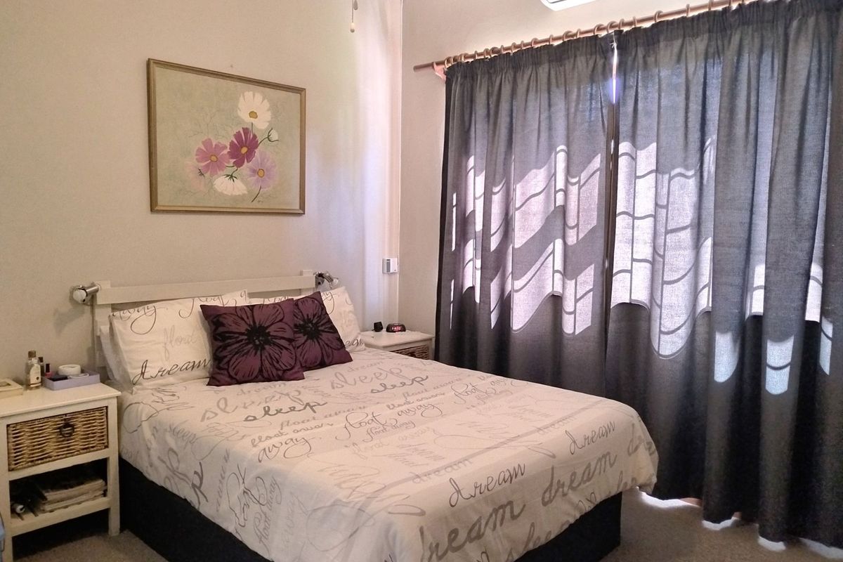 A comfortable bedroom featuring a wall-mounted air conditioning unit and large window with curtain tracks.
