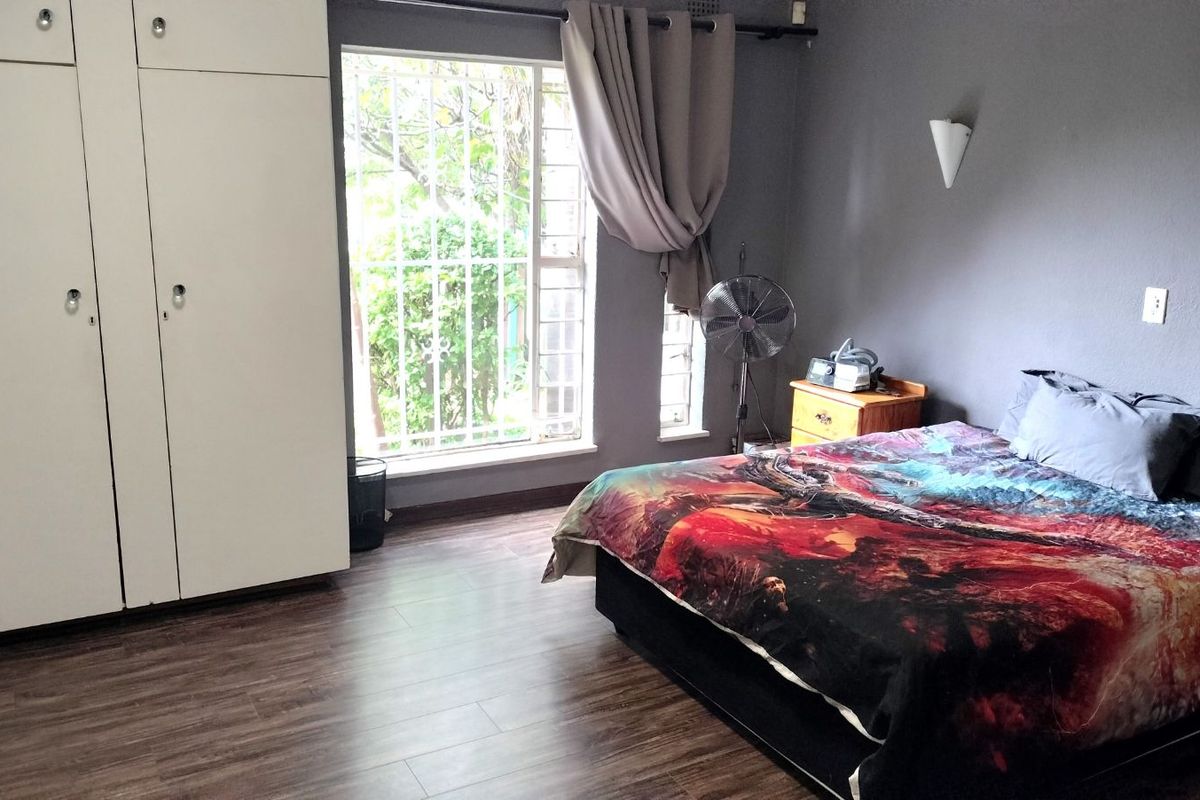 A bedroom featuring wood-look laminate flooring, built-in white cabinetry, and a window fitted with security bars.