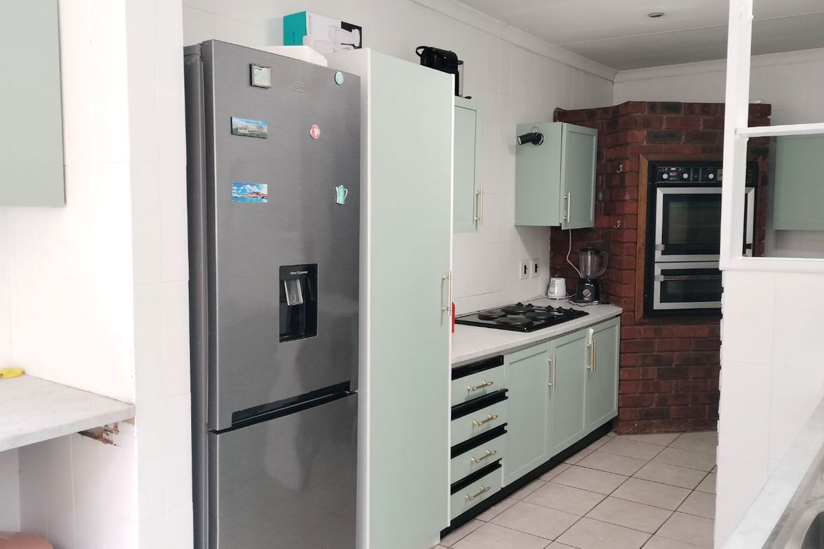 A functional kitchen featuring light green cabinetry, a built-in eye-level oven, gas hob, and tiled flooring with a brick feature wall.