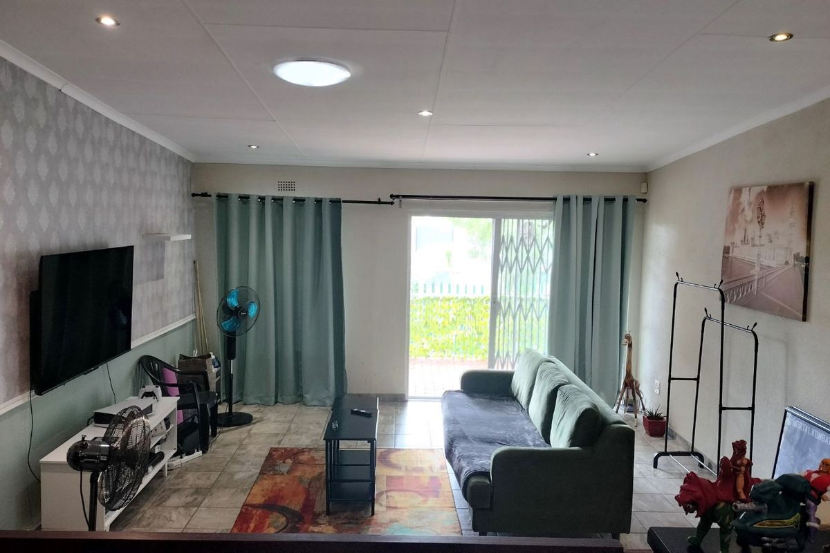 A living room featuring tiled flooring, recessed ceiling lighting, and a sliding glass door with security gate providing access to the outdoor area.