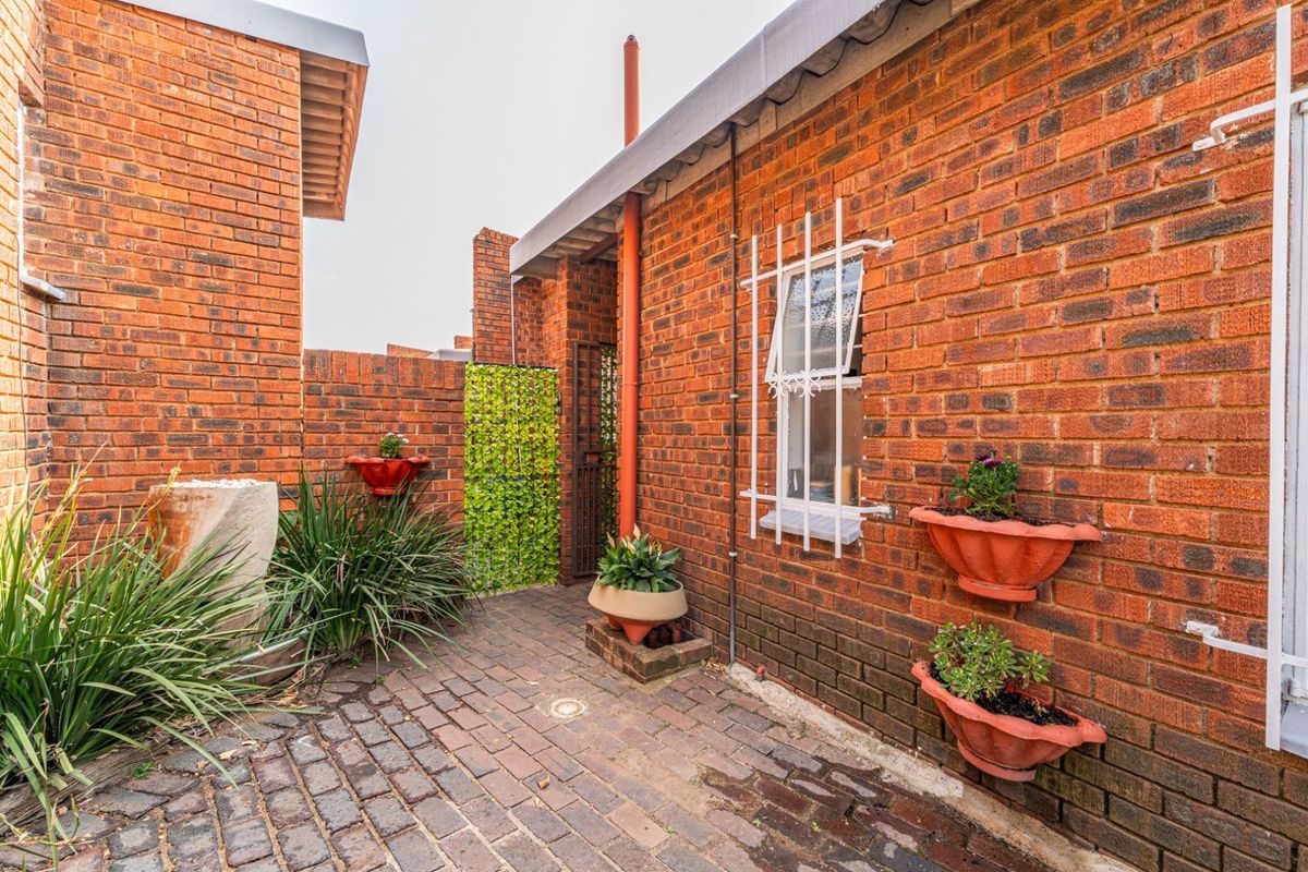 A private brick-paved courtyard area featuring exposed brick walls, a security-grilled window, and integrated drainage.