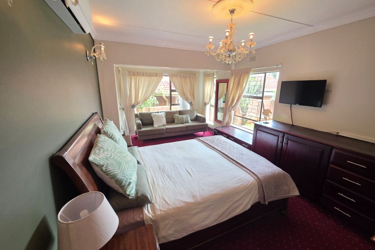 Spacious bedroom featuring a built-in dresser, wall-mounted air conditioning unit, decorative chandelier, and a cozy seating area by the window.
