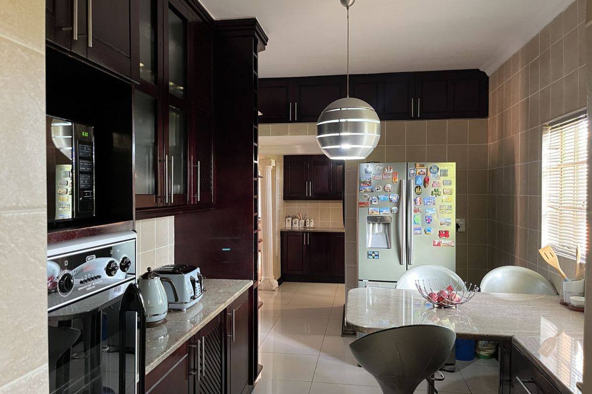 A well-appointed kitchen featuring dark wood cabinetry, granite countertops, tiled walls, and a built-in oven, with an adjacent dining area.