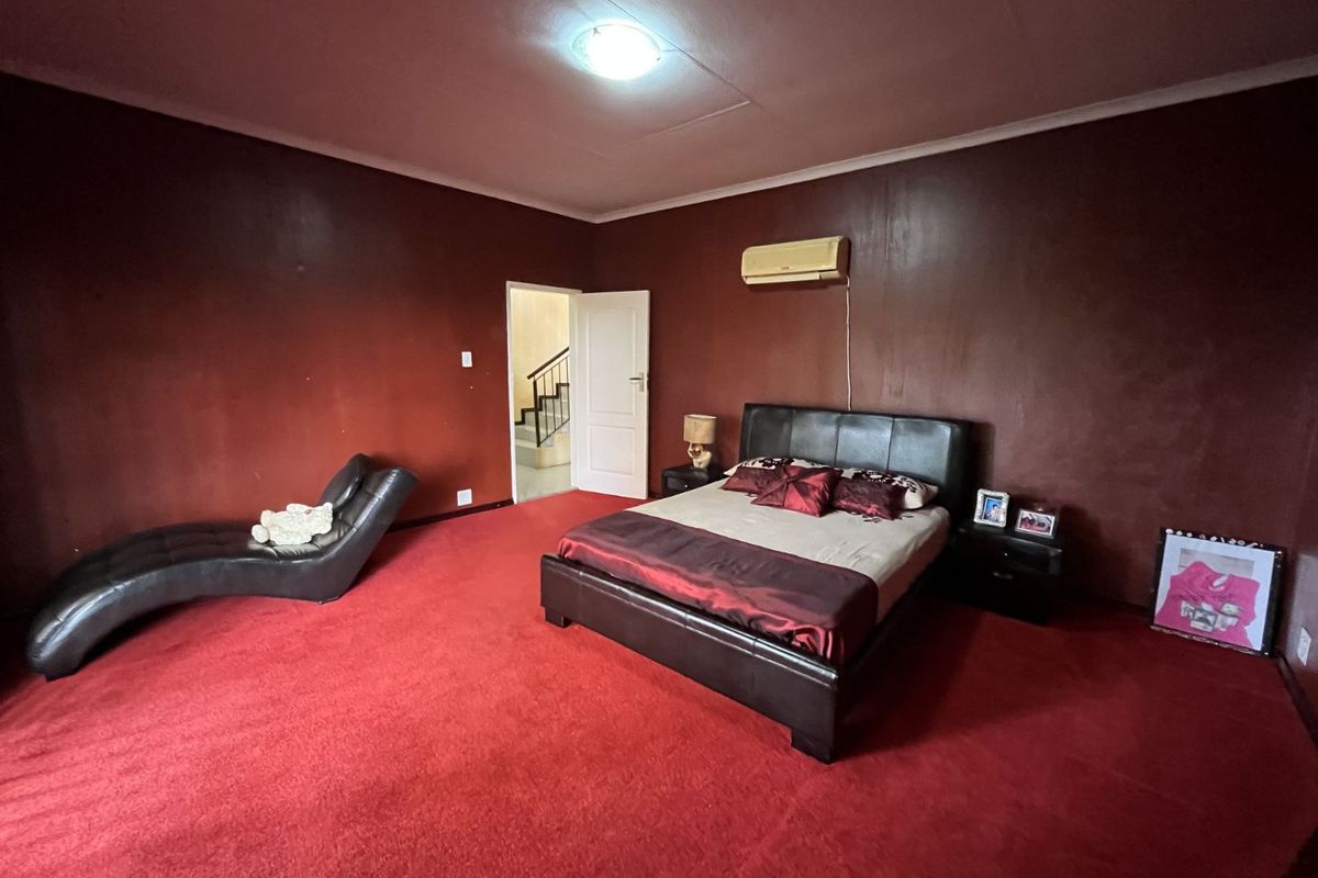 Spacious bedroom featuring red carpeting, dark wall finishes, and a wall-mounted air conditioning unit.